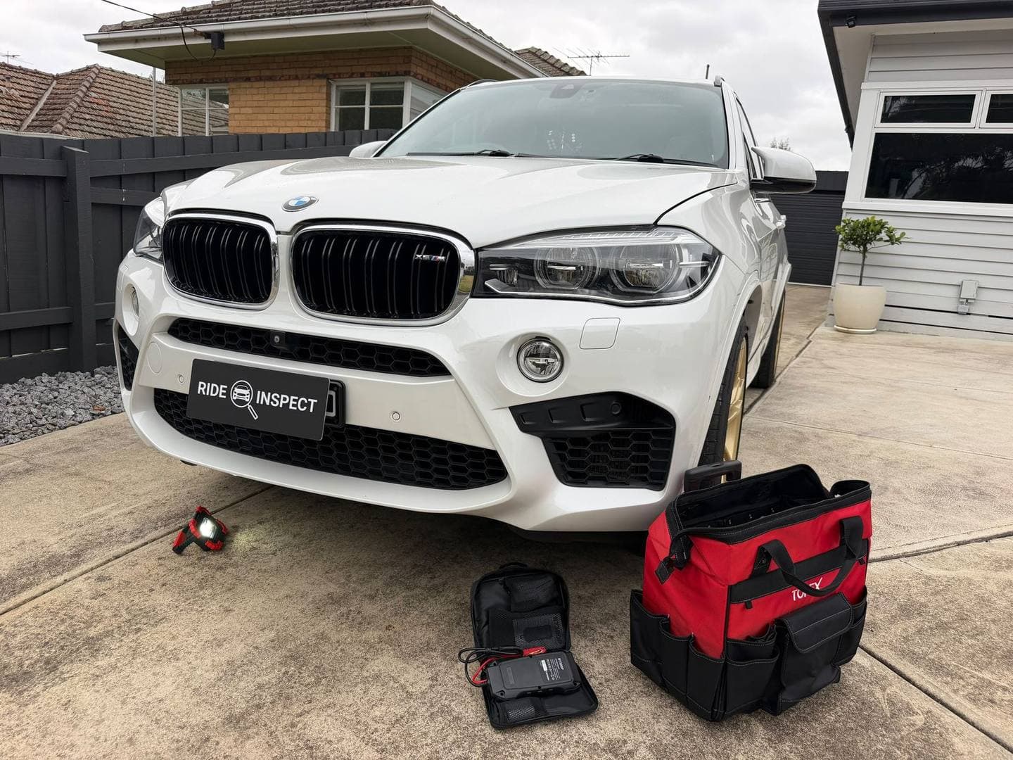 White BMW X5 M in a home driveway with the mechanic's tool bag and test kit on the ground