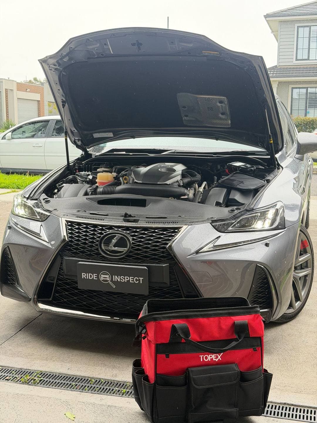 Grey Lexus IS sedan with the bonnet up outside a house, the tool bag in front