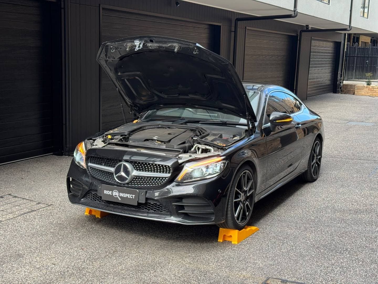 Black Mercedes-Benz C-Class coupe with the bonnet up in a townhouse driveway