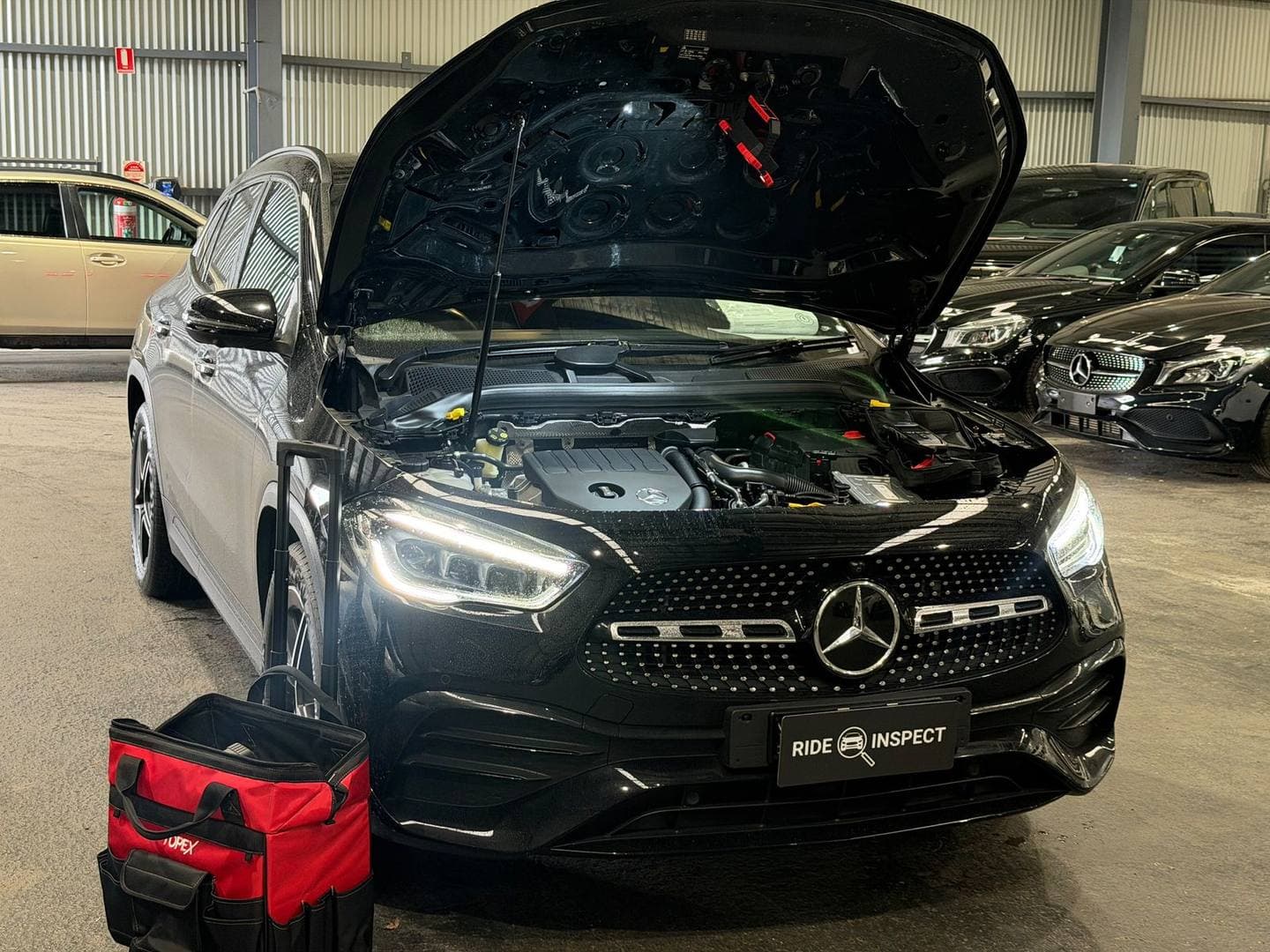 Black Mercedes-Benz GLA with the bonnet up inside a dealer showroom, the tool bag in front