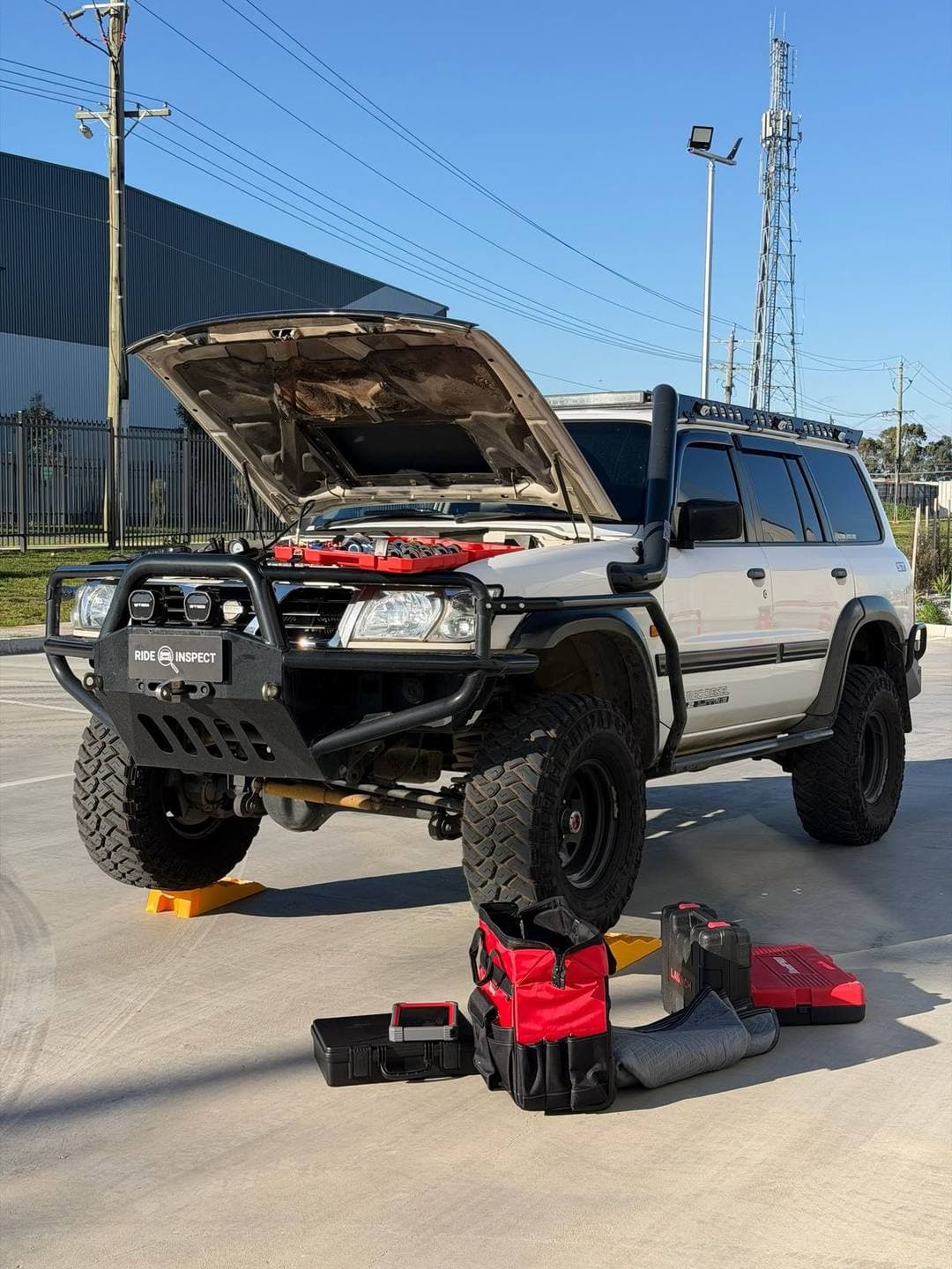 Lifted Nissan Patrol 4WD with a bullbar and snorkel, bonnet up, with tool cases laid out in front